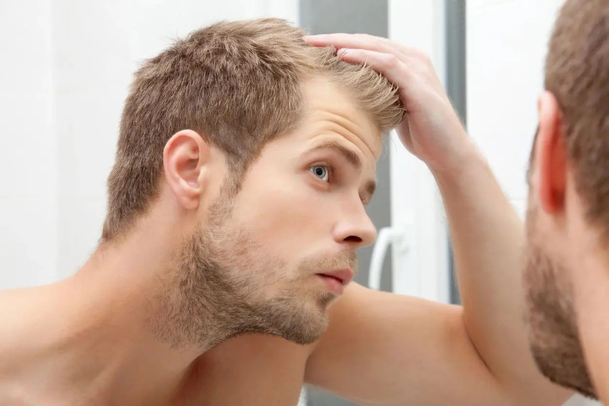 A man with his hand on his head looking at the mirror.